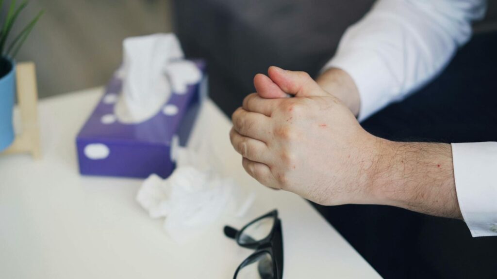 Hands nervously clasped near a tissue box, suggesting emotional stress or therapy session.