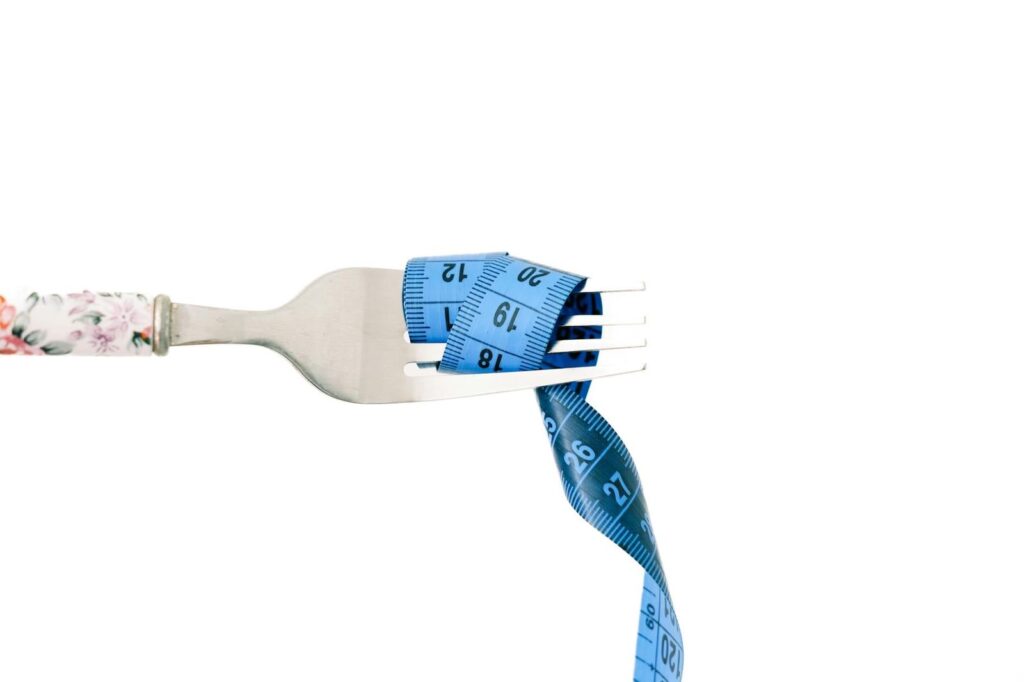 A close-up of a fork wrapped in blue measuring tape, symbolizing diet and weight management.