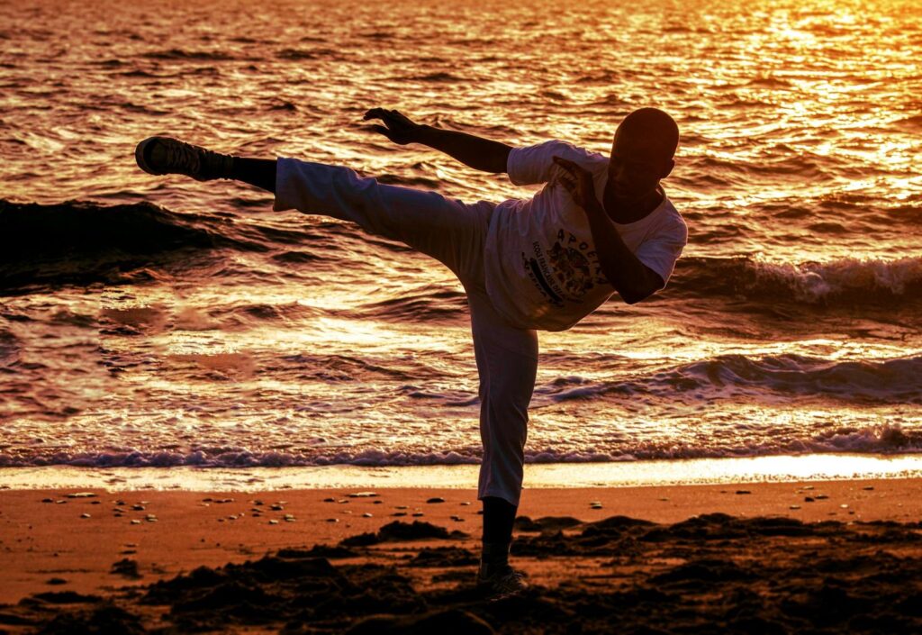 Martial artist practicing a high kick at sunset on Dakar beach, Senegal.