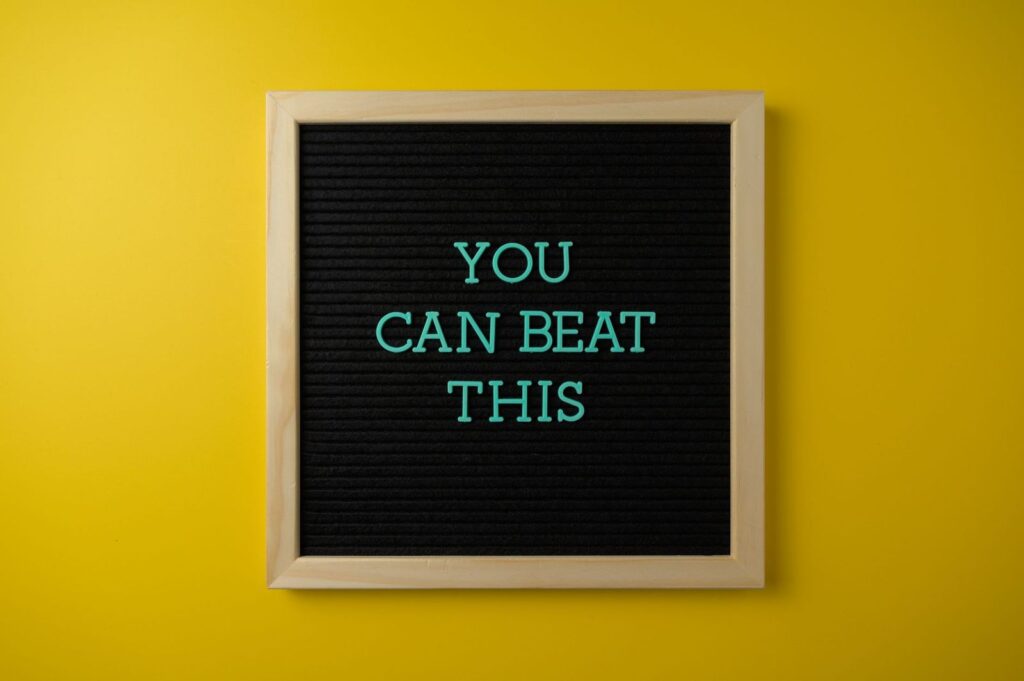 Black letter board with motivational phrase 'You Can Beat This' on vibrant yellow background.